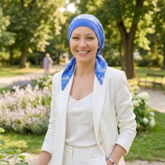 Usmievajúca sa žena v bielom kostýme v parku, na hlave modrá saténová onko šatka Canaver Belia Malena.